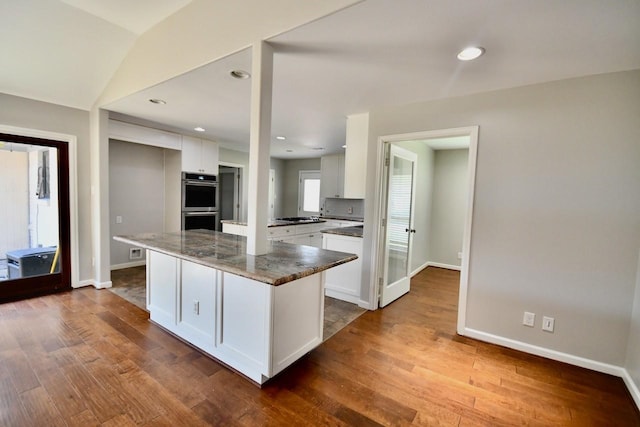 kitchen featuring stainless steel appliances, white cabinetry, hardwood / wood-style flooring, and dark stone countertops