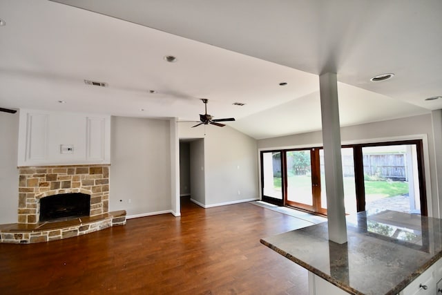 unfurnished living room featuring a stone fireplace, ceiling fan, dark hardwood / wood-style flooring, and vaulted ceiling