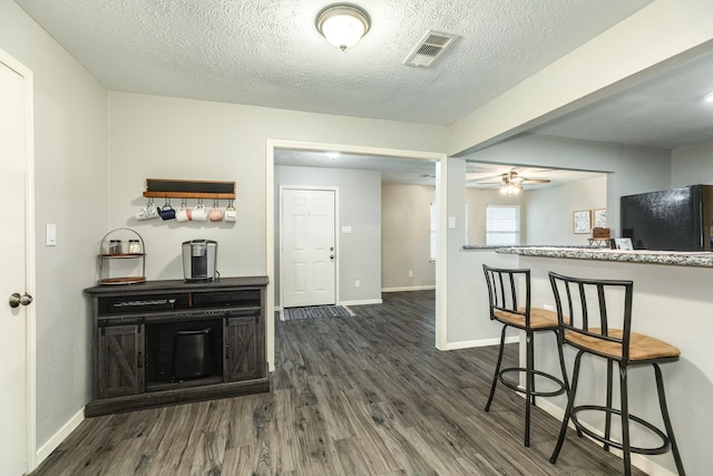 kitchen with a kitchen breakfast bar, black fridge, a textured ceiling, ceiling fan, and dark wood-type flooring