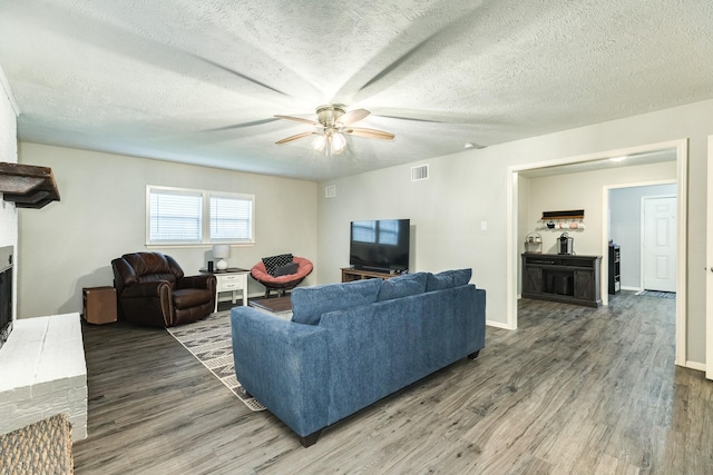 living room with a textured ceiling, ceiling fan, dark hardwood / wood-style floors, and a fireplace