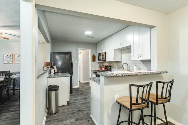 kitchen with white cabinetry, stainless steel range with gas cooktop, dark hardwood / wood-style floors, kitchen peninsula, and a kitchen bar