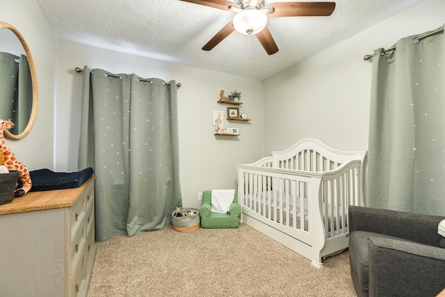 bedroom with light carpet, a textured ceiling, a nursery area, and ceiling fan