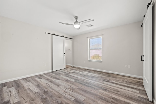 unfurnished bedroom featuring ceiling fan, a barn door, and light hardwood / wood-style floors