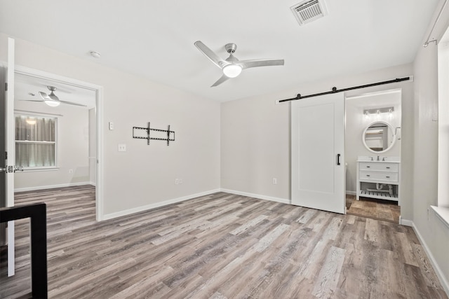 unfurnished bedroom featuring ceiling fan, a barn door, and light hardwood / wood-style floors