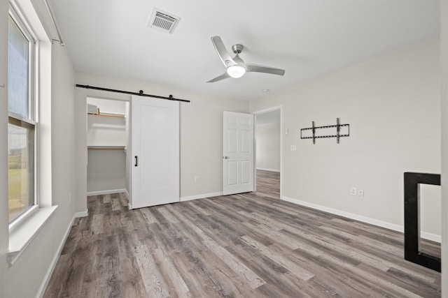 unfurnished bedroom featuring light hardwood / wood-style flooring, ceiling fan, a barn door, a spacious closet, and a closet