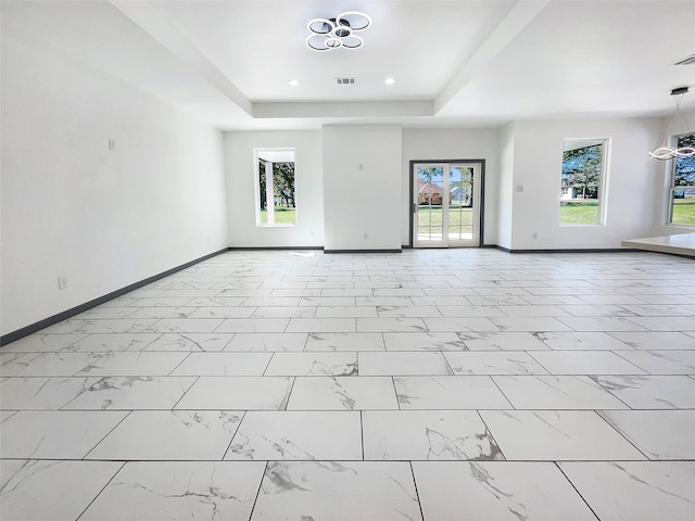 spare room featuring a tray ceiling and a chandelier