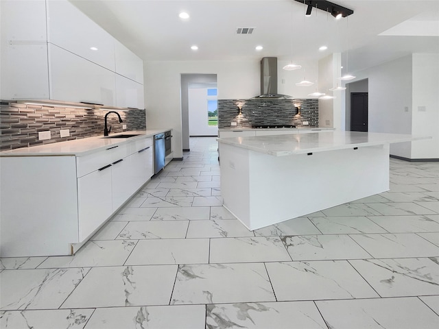 kitchen featuring pendant lighting, backsplash, wall chimney range hood, sink, and white cabinetry