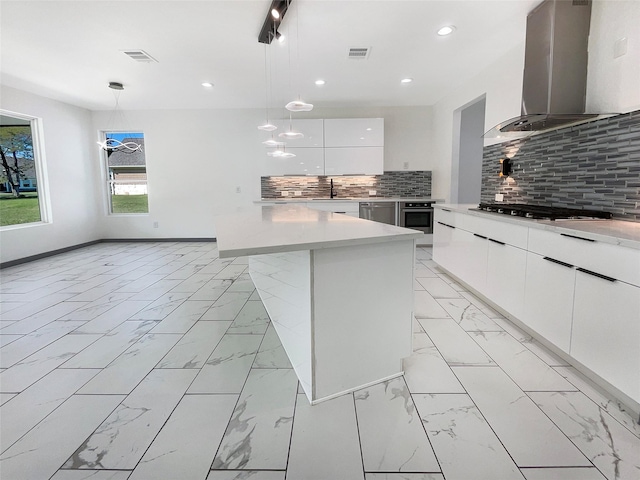 kitchen with wall chimney exhaust hood, stainless steel appliances, backsplash, decorative light fixtures, and a kitchen island