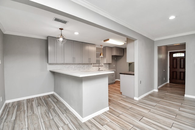 kitchen featuring decorative light fixtures, backsplash, kitchen peninsula, ornamental molding, and gray cabinetry