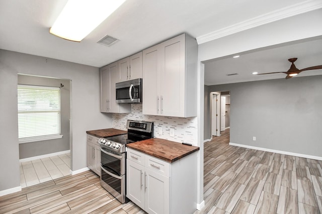 kitchen with appliances with stainless steel finishes, wooden counters, white cabinetry, tasteful backsplash, and ceiling fan