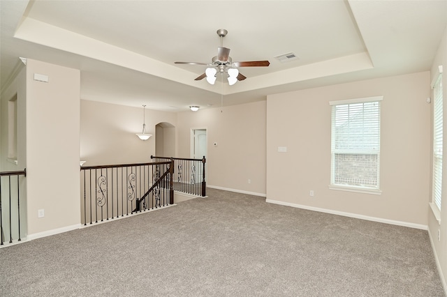 empty room featuring carpet flooring, a raised ceiling, and ceiling fan