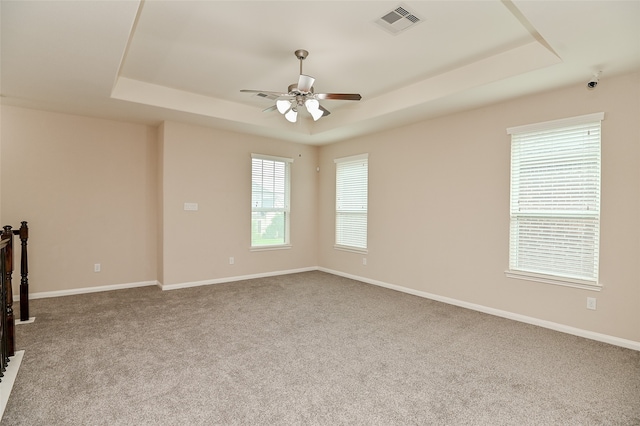 unfurnished room with ceiling fan, a raised ceiling, and light colored carpet