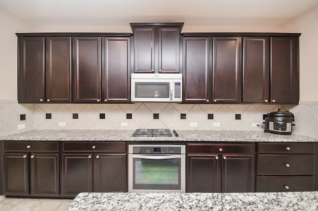 kitchen with appliances with stainless steel finishes, dark brown cabinetry, tasteful backsplash, and light stone counters