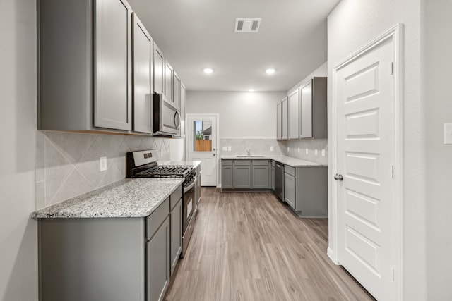 kitchen featuring decorative backsplash, appliances with stainless steel finishes, light wood-type flooring, light stone counters, and gray cabinets