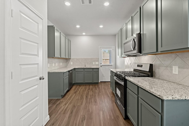 kitchen featuring dark wood-type flooring, gray cabinetry, tasteful backsplash, light stone counters, and stainless steel appliances