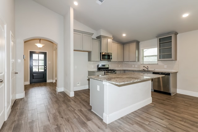 kitchen with a kitchen island, stainless steel appliances, vaulted ceiling, and light wood-type flooring