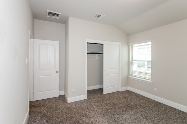 unfurnished bedroom with dark colored carpet, a closet, and lofted ceiling