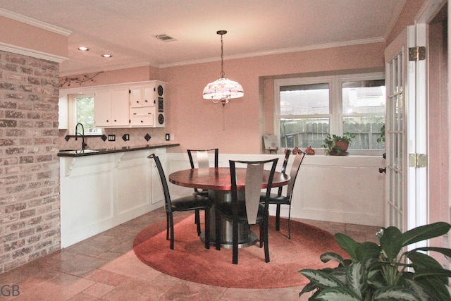 dining area with crown molding, sink, a healthy amount of sunlight, and brick wall