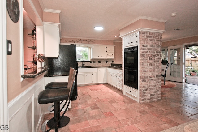 kitchen featuring decorative backsplash, black double oven, crown molding, sink, and white cabinets