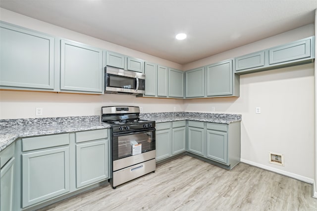 kitchen featuring baseboards, light wood-style flooring, appliances with stainless steel finishes, light stone countertops, and recessed lighting