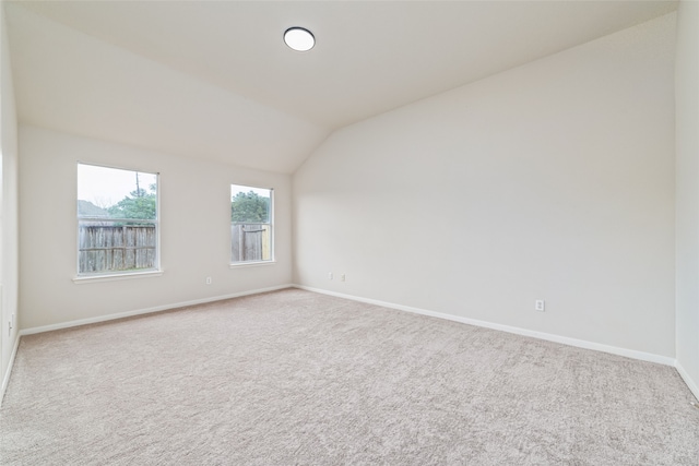 carpeted empty room with vaulted ceiling and baseboards