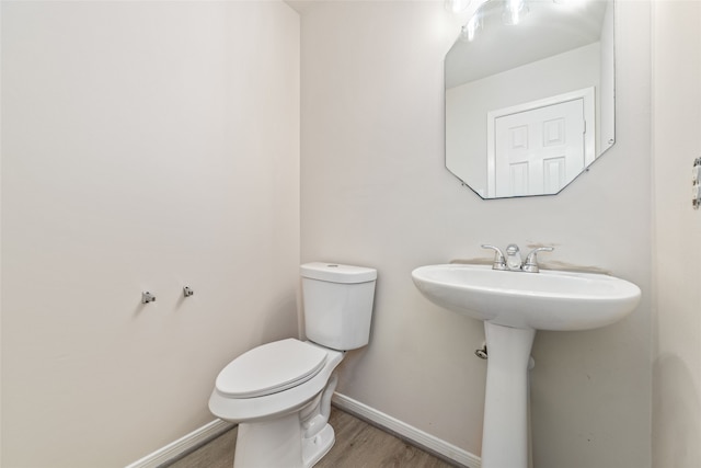 half bath with toilet, baseboards, and wood finished floors