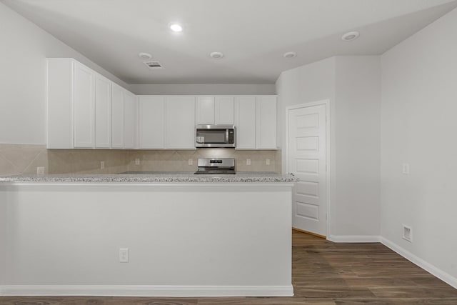 kitchen with light stone counters, dark hardwood / wood-style flooring, stainless steel appliances, decorative backsplash, and white cabinets