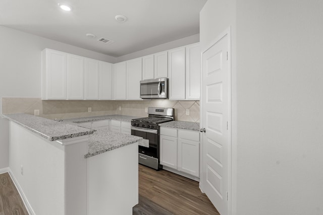 kitchen with white cabinetry, appliances with stainless steel finishes, dark hardwood / wood-style floors, kitchen peninsula, and light stone countertops