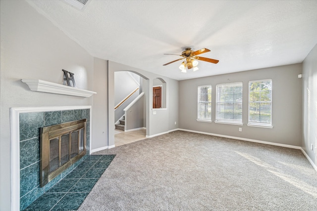 unfurnished living room with a tiled fireplace, ceiling fan, dark carpet, and a textured ceiling