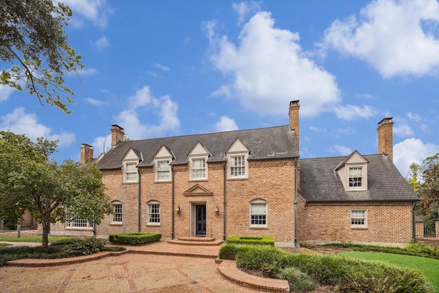 view of front of home with a high end roof, brick siding, and a chimney