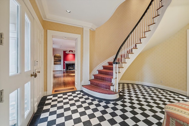 entrance foyer featuring a fireplace, wallpapered walls, ornamental molding, baseboards, and stairs