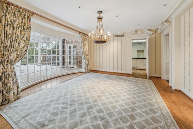 empty room featuring wood finished floors, visible vents, baseboards, ornamental molding, and an inviting chandelier