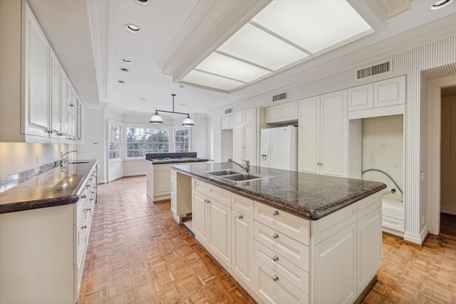 kitchen with crown molding, sink, white fridge with ice dispenser, an island with sink, and white cabinetry