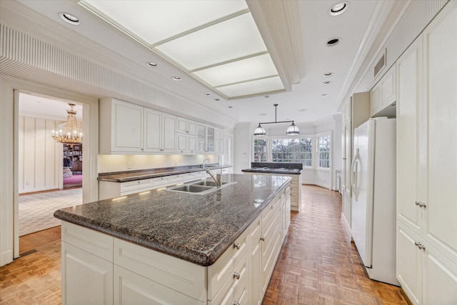 kitchen with visible vents, ornamental molding, a sink, an island with sink, and white fridge with ice dispenser