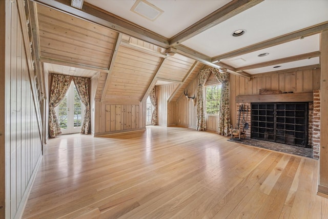 unfurnished living room featuring light wood-style floors, wood walls, lofted ceiling with beams, and a fireplace with flush hearth