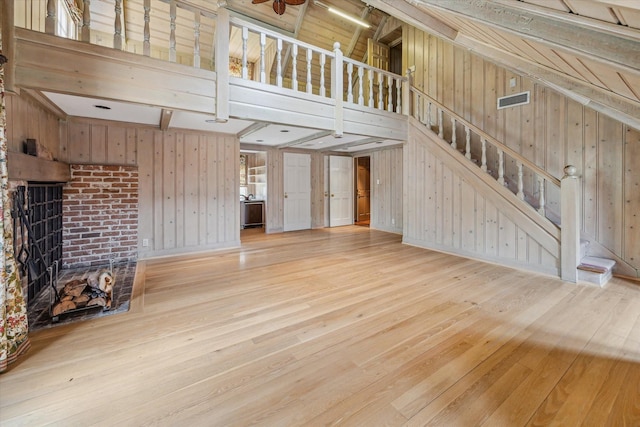 unfurnished living room featuring stairs, hardwood / wood-style floors, wood walls, and a towering ceiling