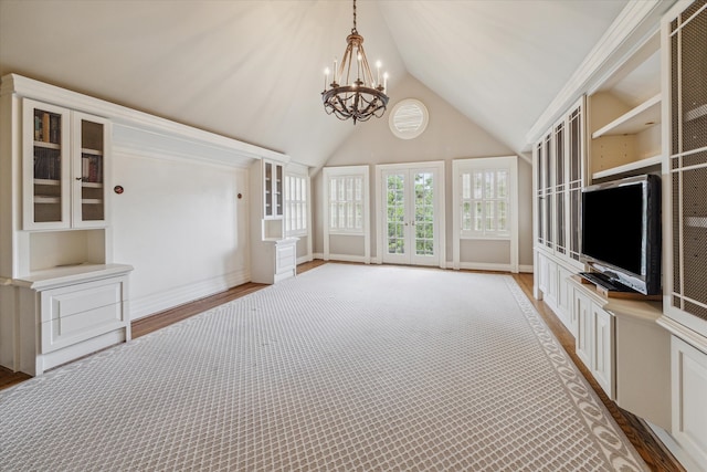 unfurnished living room featuring a notable chandelier, light hardwood / wood-style floors, french doors, and vaulted ceiling