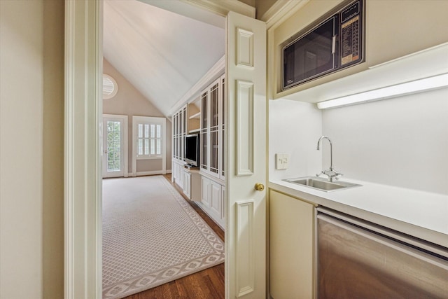 kitchen featuring lofted ceiling, dishwashing machine, wood finished floors, light countertops, and a sink