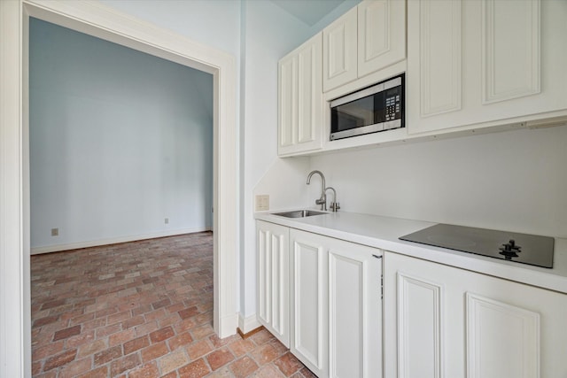 kitchen with light countertops, stainless steel microwave, a sink, baseboards, and black electric cooktop