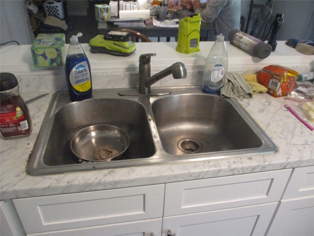 interior details featuring white cabinets, light stone countertops, and sink