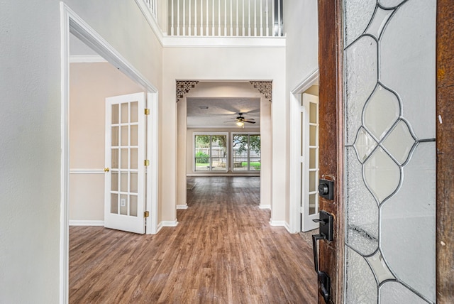 foyer entrance with ceiling fan, french doors, a high ceiling, crown molding, and wood-type flooring