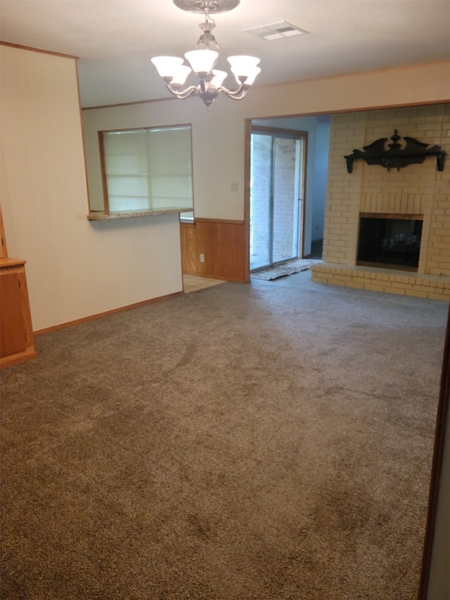 unfurnished living room with a notable chandelier, wood walls, carpet floors, and a fireplace