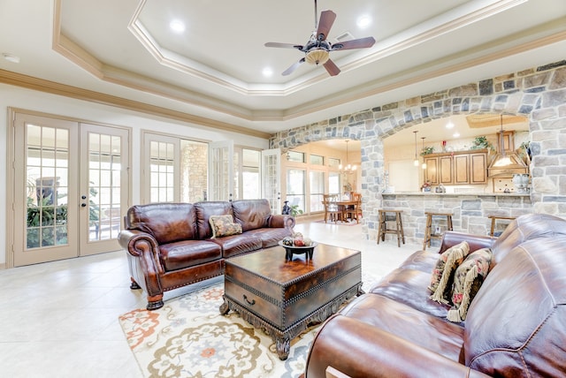 living room with ceiling fan with notable chandelier, crown molding, a tray ceiling, and french doors