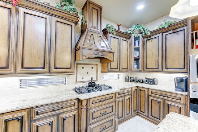 kitchen featuring light tile patterned floors, backsplash, light stone counters, and stainless steel gas cooktop