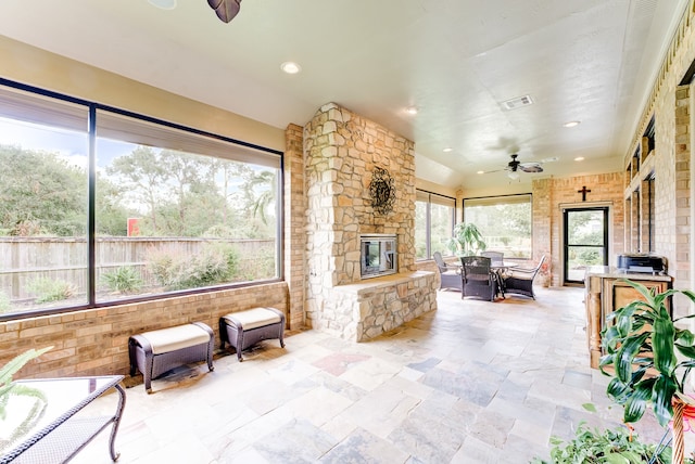 sunroom with ceiling fan and a stone fireplace