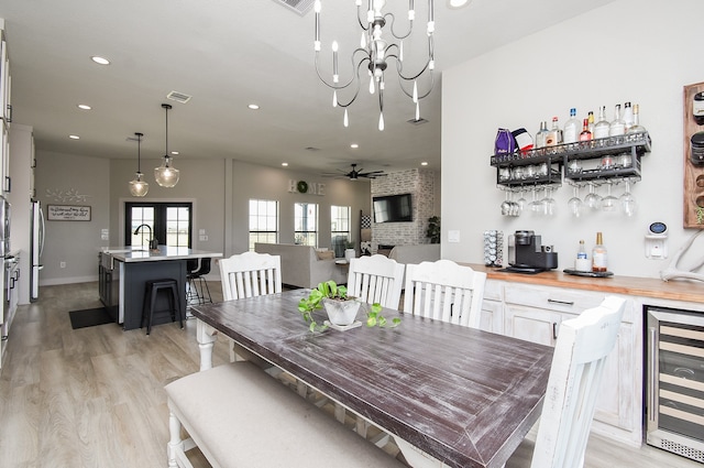 dining area with french doors, ceiling fan with notable chandelier, beverage cooler, wet bar, and light hardwood / wood-style flooring