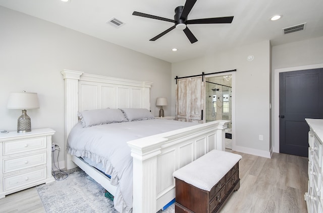 bedroom with ceiling fan, a barn door, light hardwood / wood-style floors, and ensuite bathroom