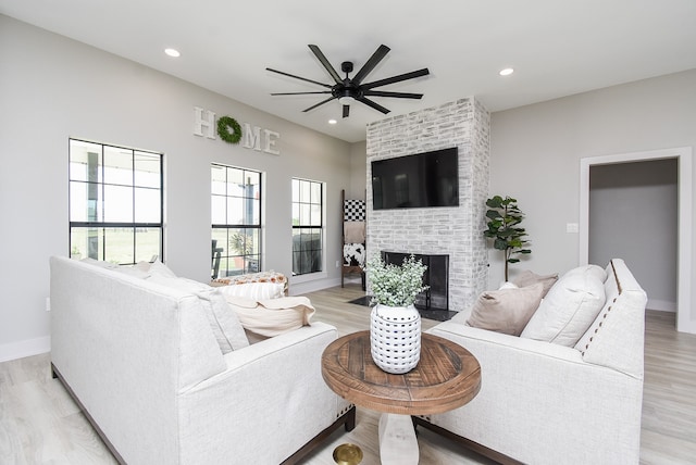 living room featuring a brick fireplace, ceiling fan, and light wood-type flooring