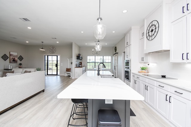 kitchen featuring white cabinets, a center island with sink, sink, and hanging light fixtures