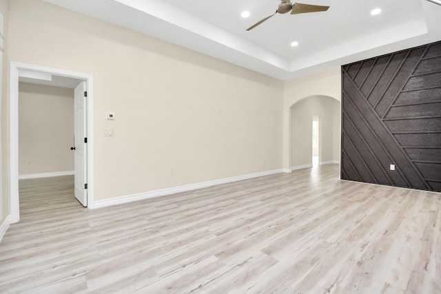 empty room with a tray ceiling, ceiling fan, and light hardwood / wood-style flooring